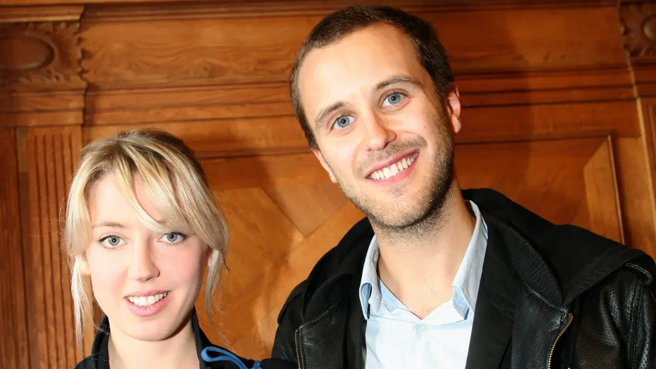 Oskar Linnros och Veronica Maggio ler mot kameran, med en träbakgrund som ger en varm känsla.