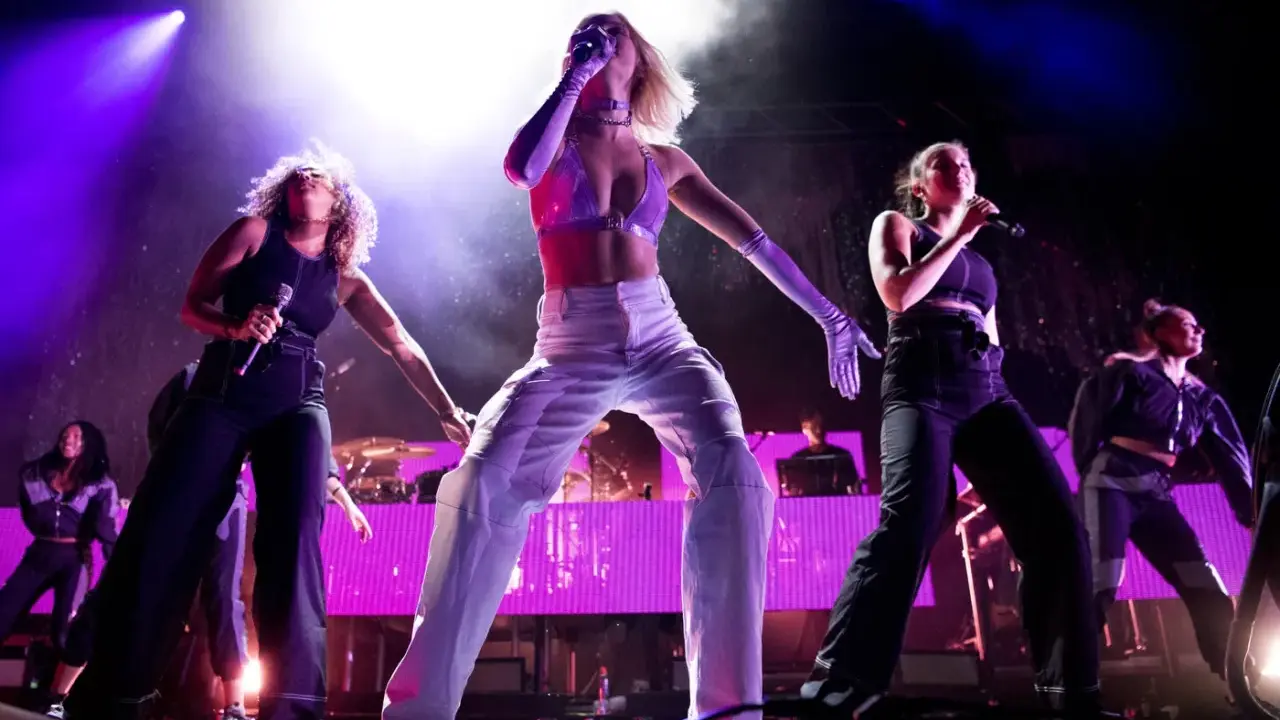 Zara Larsson and backup singers perform on stage with bright purple lighting.