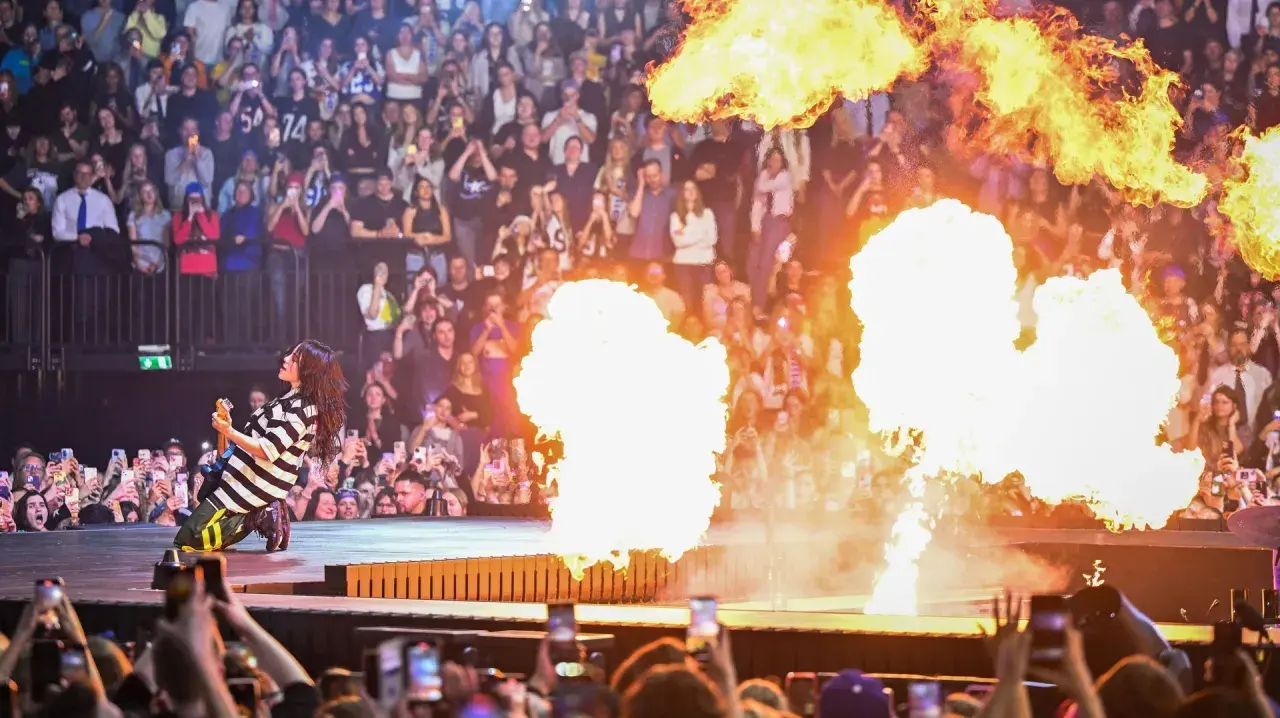 Billie Eilish ger en elektrisk Billie Eilish konsert med flammor som exploderar runt henne. Publiken filmar med sina mobiler.