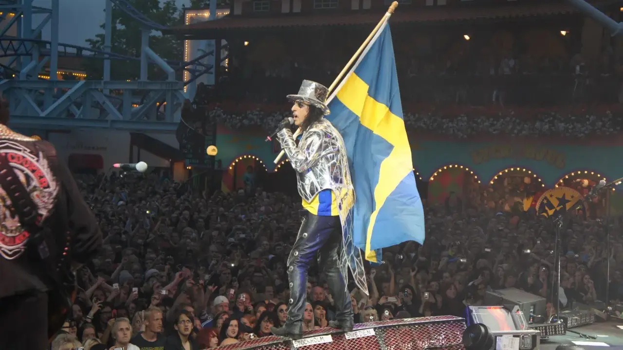 Alice Cooper i Sverige, med svensk flagga och en stor publik som filmar.