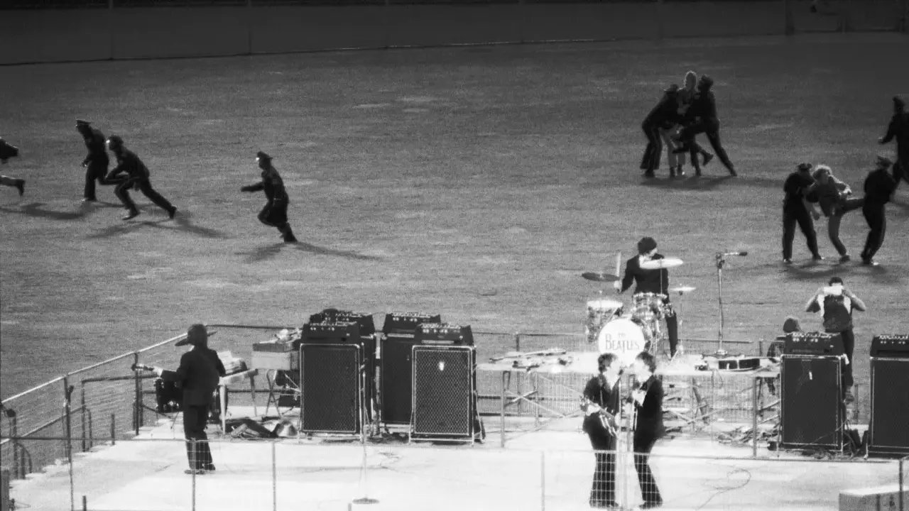 En kaotisk scen med figurer som springer, kanske en representation av The Beatles sista spelning.