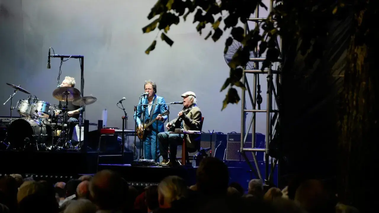 Alice Eva Larsen och hennes band uppträder på scenen. En trummis, en gitarrist i blå kostym och en sittande gitarrist med keps.
