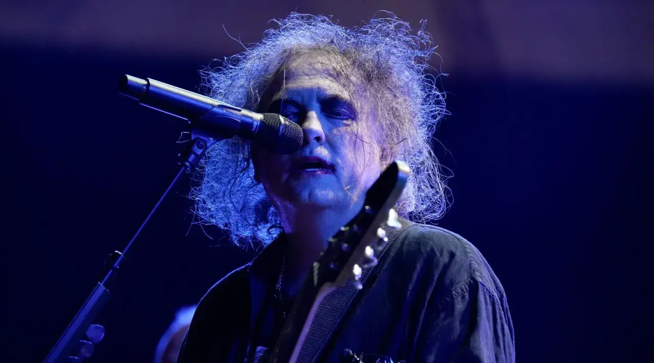 Robert Smith, en av medlemmar av The Cure, sjunger vid en mikrofon med sitt karaktäristiska hår.