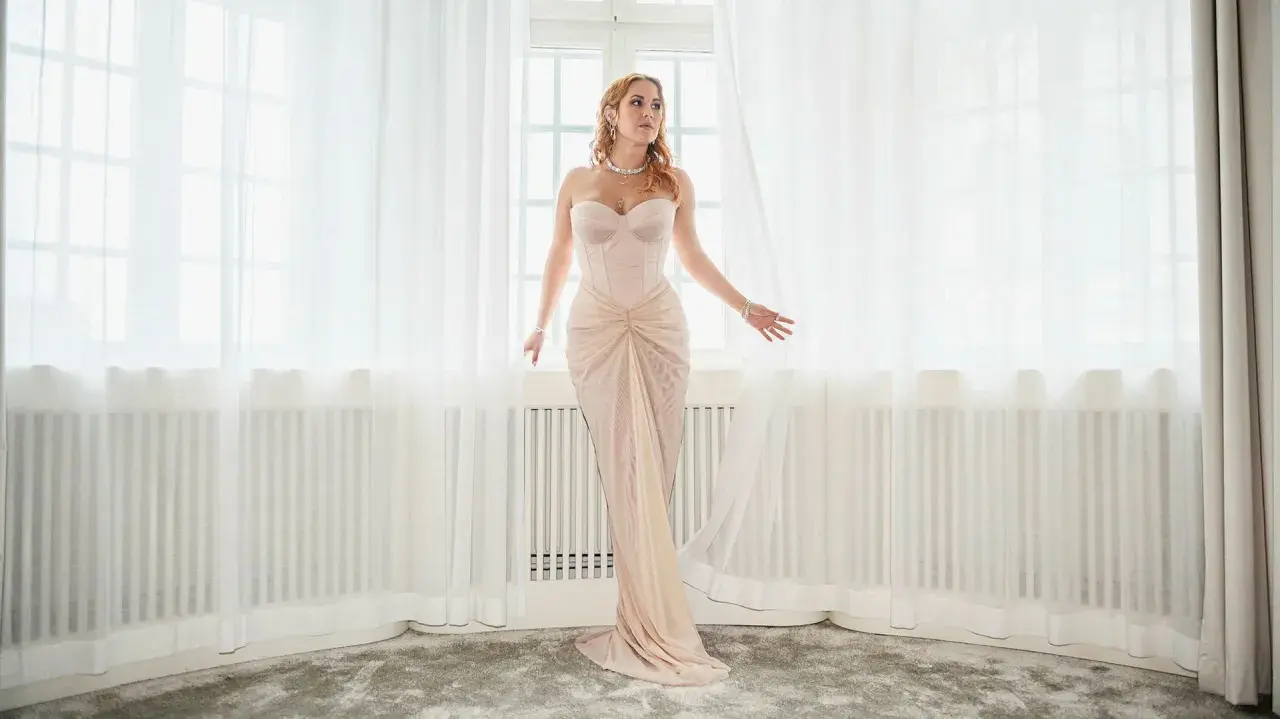 Molly Sandén i en ljusrosa klänning vid ett fönster, redo för Elle-galan.
