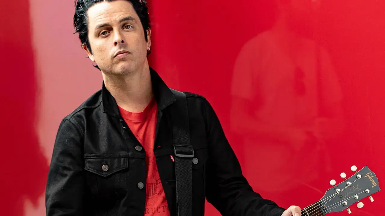 Billie Joe Armstrong, green day sångare, med sin Gibson Les Paul gitarr mot en röd bakgrund.