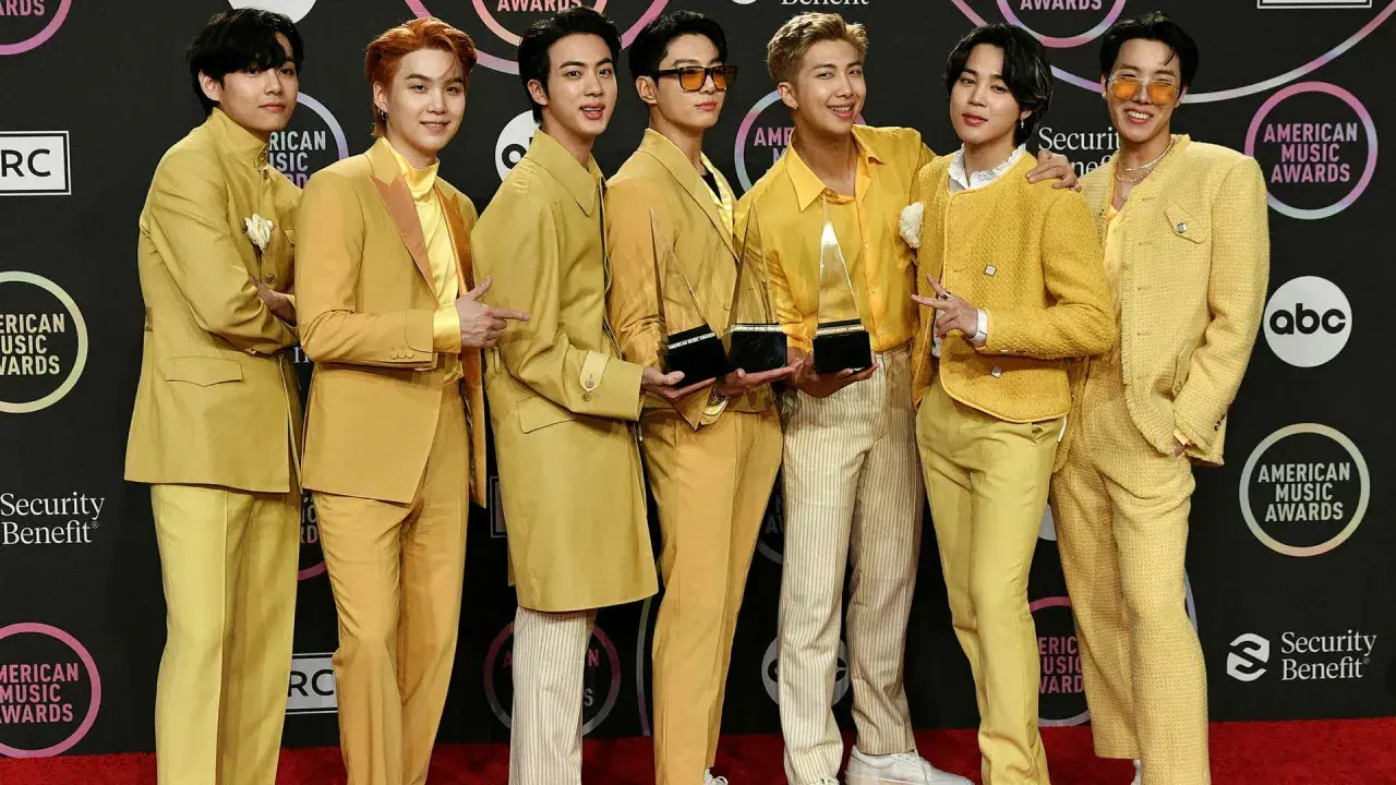 Medlemmar av BTS poserar glatt på röda mattan, klädda i matchande gula outfits och håller sina American Music Awards-troféer.
