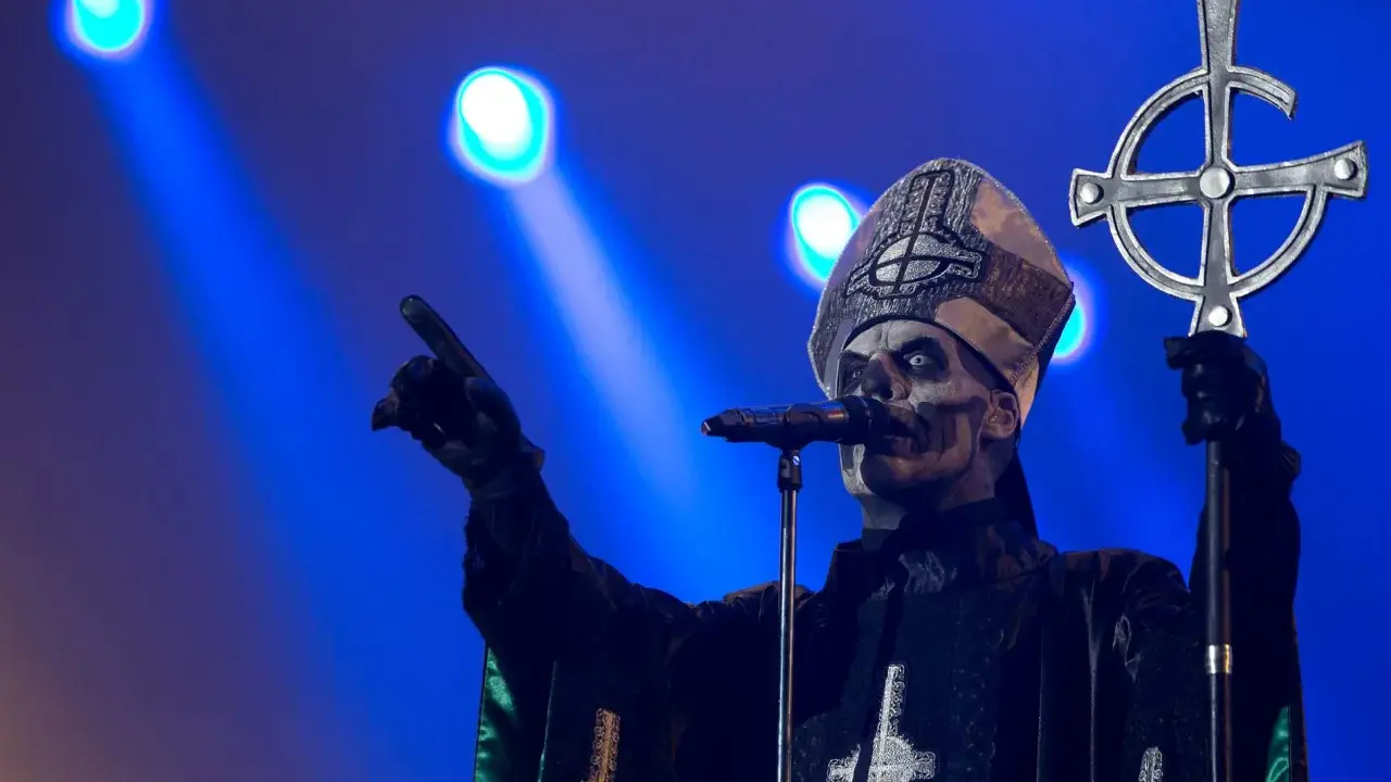 Jocke Berg som Papa Emeritus IV från Ghost, med vit ansiktsmålning och en korsstav, pekar mot publiken under en konsert.