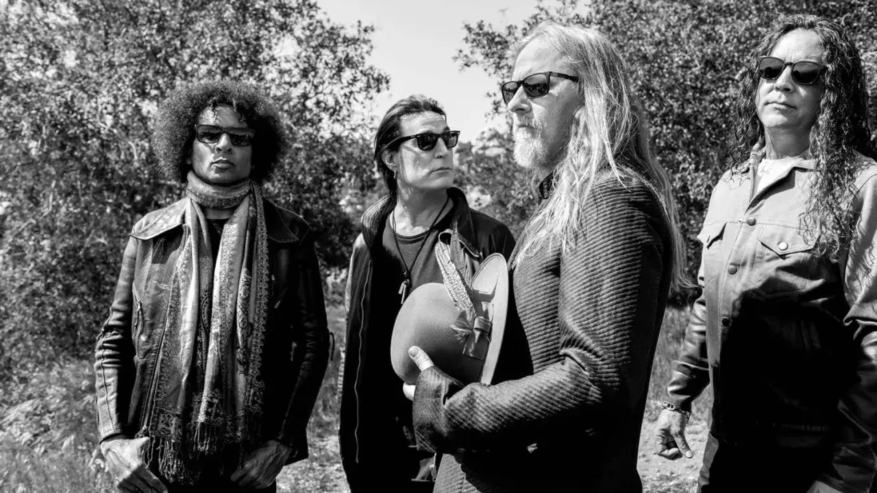 Medlemmar av Alice in Chains, fyra män med solglasögon, står utomhus bland träd. En håller en hatt med fjädrar.