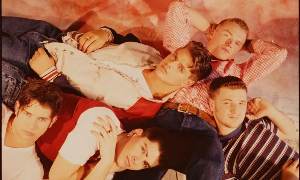 Medlemmar av Boyzone ligger tätt tillsammans, klädda i jeans och färgglada toppar.