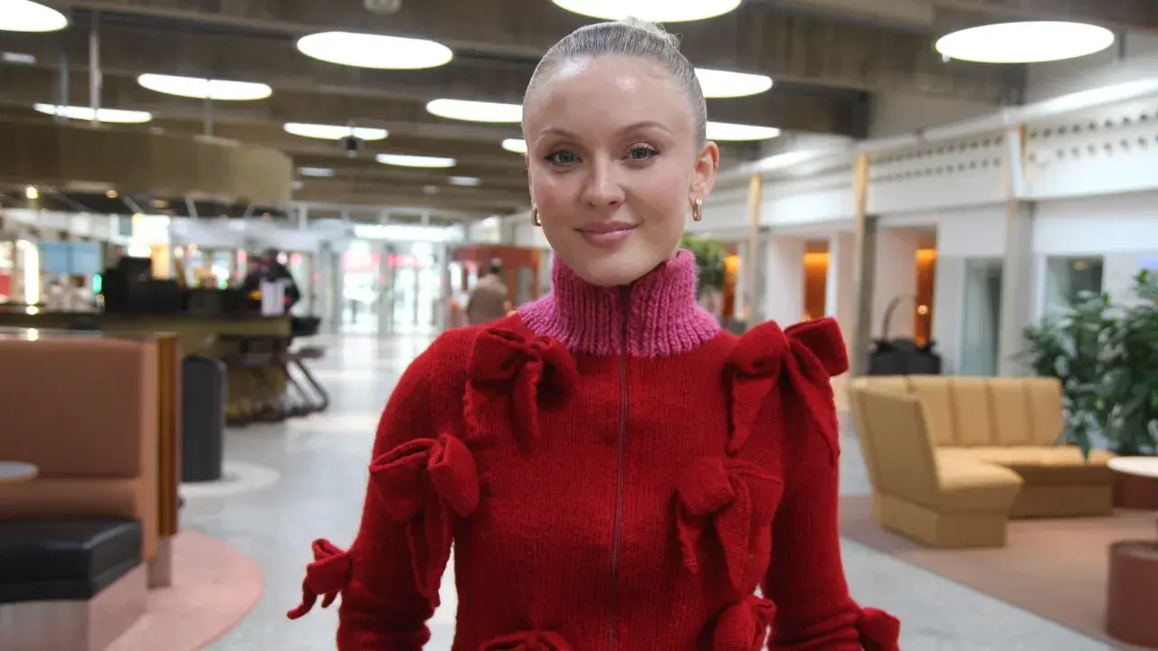 Zara Larsson i USA, klädd i en röd tröja med rosetter, ler mot kameran.