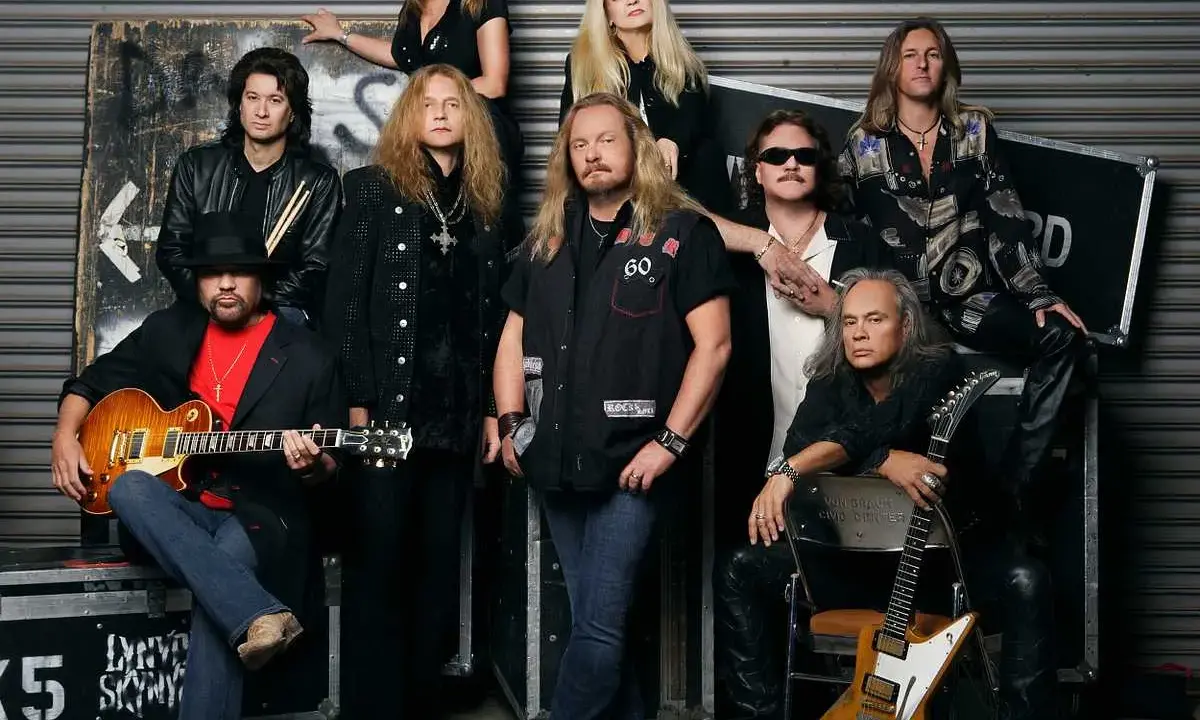 Medlemmar av Lynyrd Skynyrd poserar för ett gruppfoto. En man i förgrunden håller en gitarr.