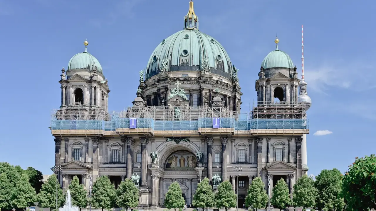 Berlins domkyrka med sina imponerande kupoler är ett måste när man undrar vad ska man se i Berlin. En fontän och grönskande träd ramar in den vackra byggnaden.