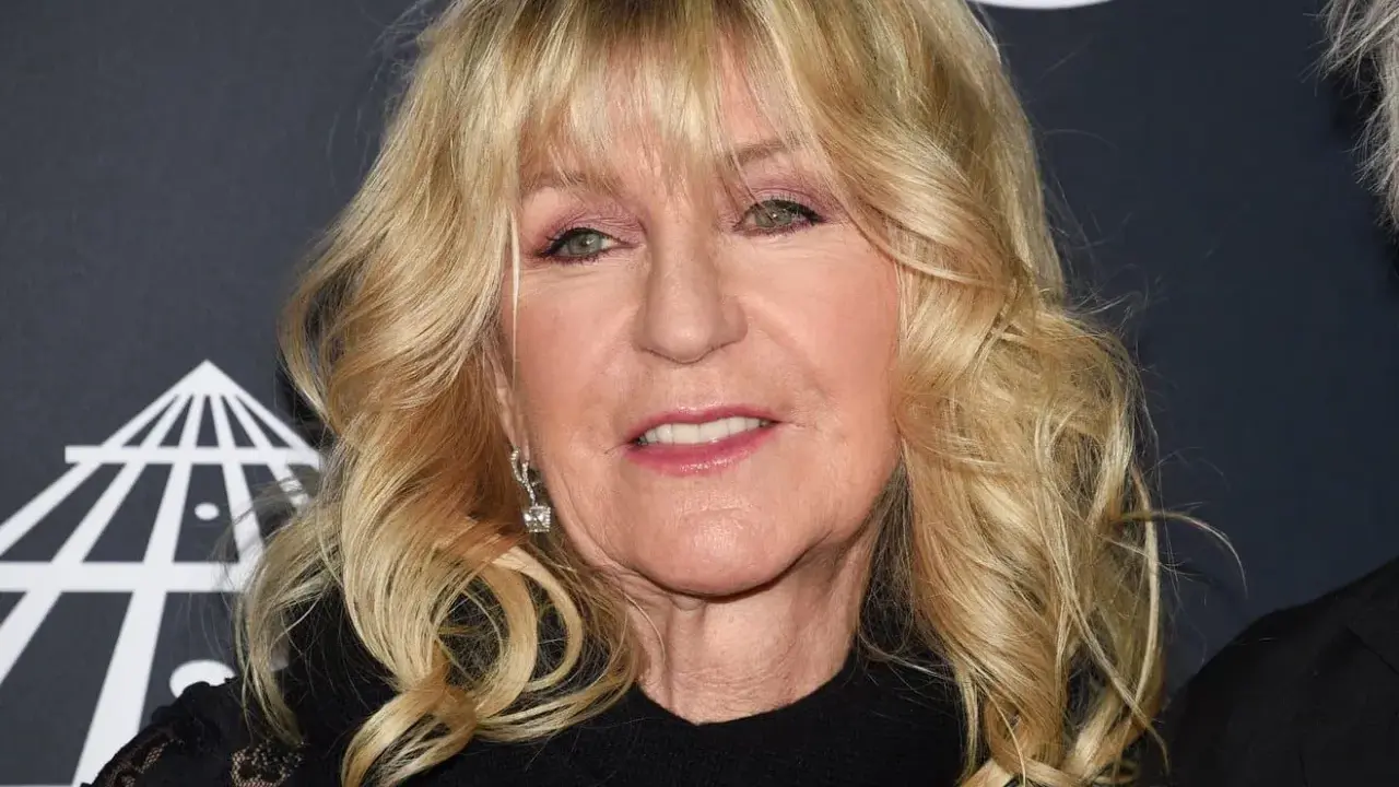 Christine McVie, en ikonisk sångerska i Fleetwood Mac, ler med sitt blonda hår och smycken.