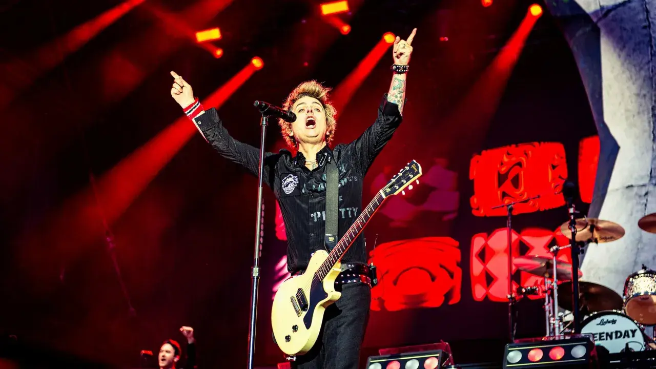 Billie Joe Armstrong, en av medlemmar av Green Day, sjunger och spelar gitarr på scenen under en konsert, upplyst av röda strålkastare.