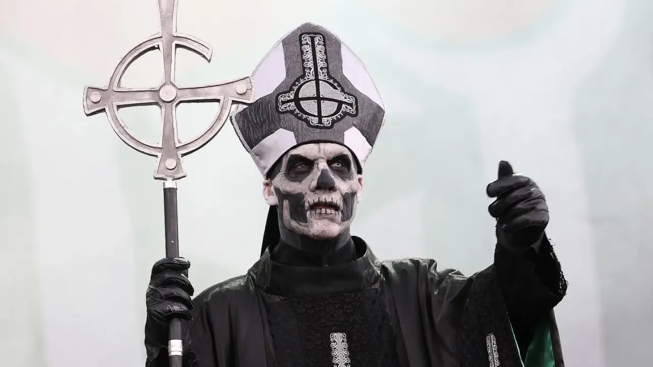 Tobias Forge som Papa Emeritus IV, med sin ikoniska sminkning och påvehatt, håller en korsstav. Han påminner om en kuslig onkel Kånkel.
