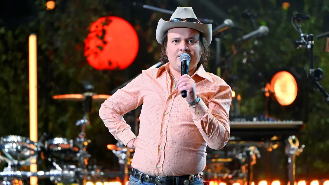 David Ritschard konsert. Artist med cowboyhatt och orange mönstrad skjorta sjunger i mikrofon på scenen.