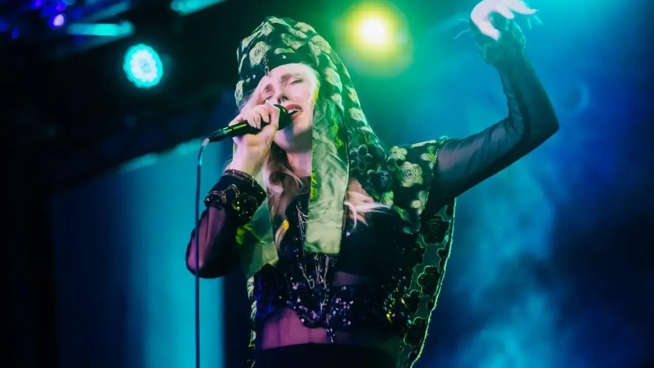 Amanda Jenssen konsert. Hon sjunger med en mikrofon i handen, klädd i en blommig scarf och en glittrig topp.