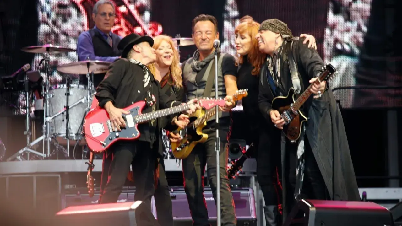 Medlemmar av E Street Band på scen, med Bruce Springsteen i mitten, omgiven av bandmedlemmar som spelar gitarr.