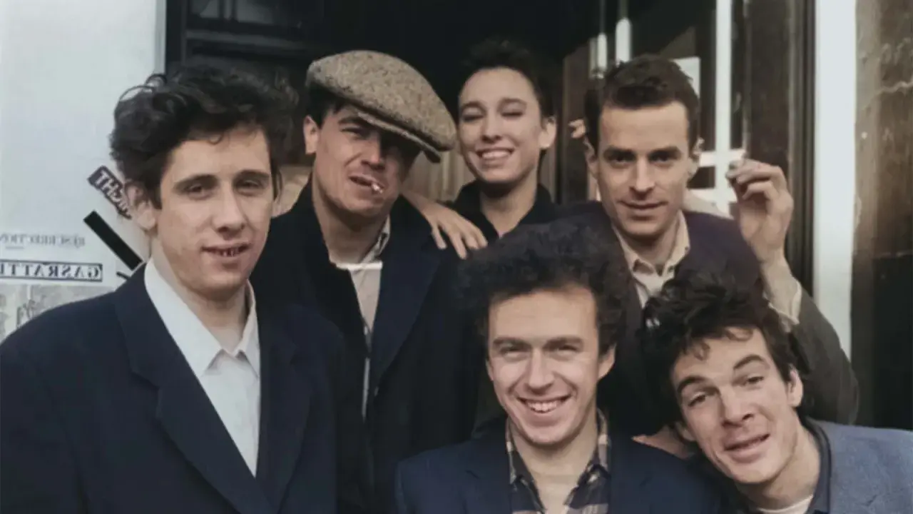 Medlemmar av the Pogues poserar glatt utomhus, några med cigaretter.