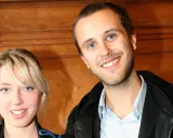 Oskar Linnros och Veronica Maggio ler mot kameran, med en träbakgrund som ger en varm känsla.