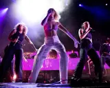 Zara Larsson and backup singers perform on stage with bright purple lighting.