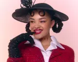 Daniela Rathana med en svart hatt och röd kavaj, med glittriga handskar och en lekfull blick.