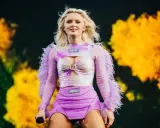 Zara Larsson konsert. Hon står på scenen i en lila och rosa outfit med fjädrar på ärmarna.