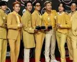 Medlemmar av BTS poserar glatt på röda mattan, klädda i matchande gula outfits och håller sina American Music Awards-troféer.