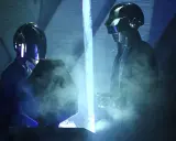 Medlemmar av Daft Punk i sina ikoniska hjälmar, omgivna av rök och blått ljus på scenen.