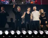Medlemmar av Panic! at the Disco på scenen, en gör hjärta med händerna, en annan vinkar med två fingrar.