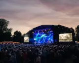 Stor publik vid Rosendal Garden Party. En scen med blå ljus och artister, omgiven av träd och en vacker kvällshimmel.