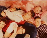 Medlemmar av Boyzone ligger tätt tillsammans, klädda i jeans och färgglada toppar.