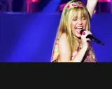 Miley Cyrus sjunger med ett stort leende på scenen i Sverige, iklädd en färgglad topp och pannband.