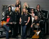 Medlemmar av Lynyrd Skynyrd poserar för ett gruppfoto. En man i förgrunden håller en gitarr.