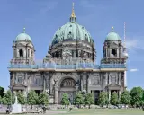 Berlins domkyrka med sina imponerande kupoler är ett måste när man undrar vad ska man se i Berlin. En fontän och grönskande träd ramar in den vackra byggnaden.