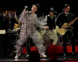 Harry Styles i glittrig outfit på en magisk harry styles konsert. Bandet spelar bakom honom, en gitarrist i kostym och en trummis.