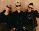 Green Day Sverige: Billie Joe Armstrong, Mike Dirnt och Tré Cool poserar framför en vägg.