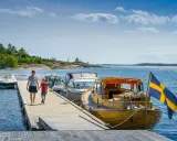 En kvinna och ett barn går på en brygga med båtar och en svensk flagga. En perfekt bild av en semester i Sverige.