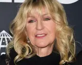 Christine McVie, en ikonisk sångerska i Fleetwood Mac, ler med sitt blonda hår och smycken.