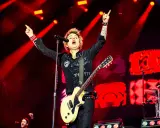 Billie Joe Armstrong, en av medlemmar av Green Day, sjunger och spelar gitarr på scenen under en konsert, upplyst av röda strålkastare.