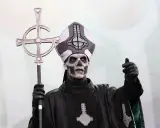Tobias Forge som Papa Emeritus IV, med sin ikoniska sminkning och påvehatt, håller en korsstav. Han påminner om en kuslig onkel Kånkel.