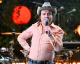 David Ritschard konsert. Artist med cowboyhatt och orange mönstrad skjorta sjunger i mikrofon på scenen.