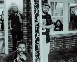 Band of Horses i Stockholm. Fyra män poserar utanför ett hus, en tittar ut genom ett fönster.