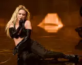 Zara Larsson sjunger på scenen i en svart outfit med glansiga handskar, som en modern tolkning av Burzum-estetik.