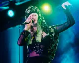 Amanda Jenssen konsert. Hon sjunger med en mikrofon i handen, klädd i en blommig scarf och en glittrig topp.