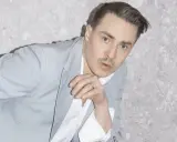 Man med blå ögon och mustasch i ljusblå kavaj. Han lutar sig mot en grå stenvägg, en tankfull blick. Fibes oh fibes.