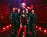 Eurovision svenska kommentatorer: artist med dansare i glänsande svarta rockar och rött, på en scen med röda ljus.