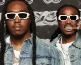 Två medlemmar av Migos, klädda i denimjackor och vita solglasögon, poserar med bling och grillz.