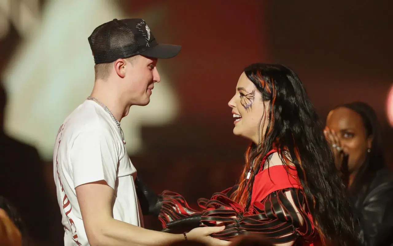 En man med keps och en kvinna med fjärilsminkning ler mot varandra under en Miriam Bryant konsert.