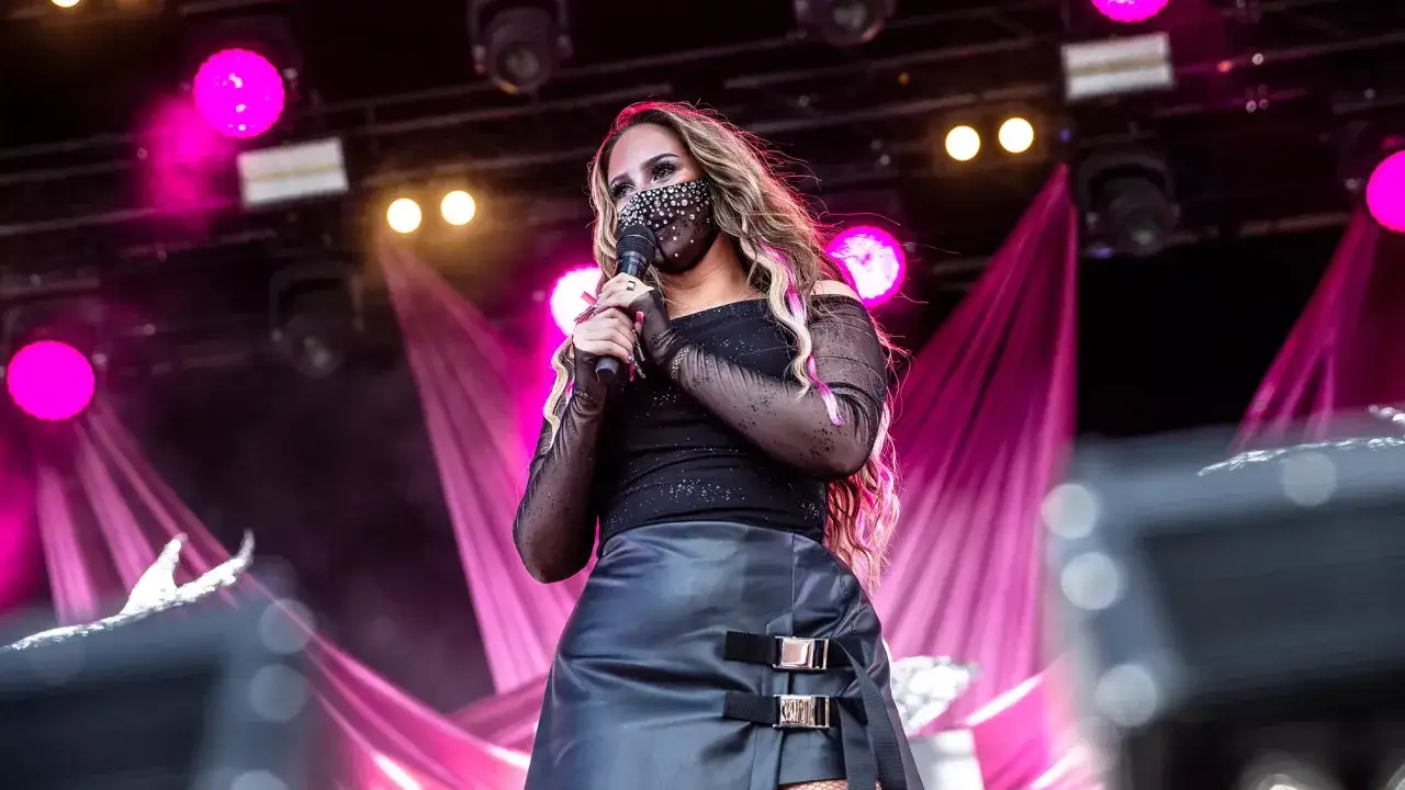 Miley Cyrus i Sverige, på scen med glittrig mask och svart outfit, badar i rosa ljus.